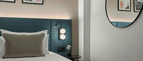 A neatly made bed with pillows, a bedside table with a lamp, and wall-mounted lights.