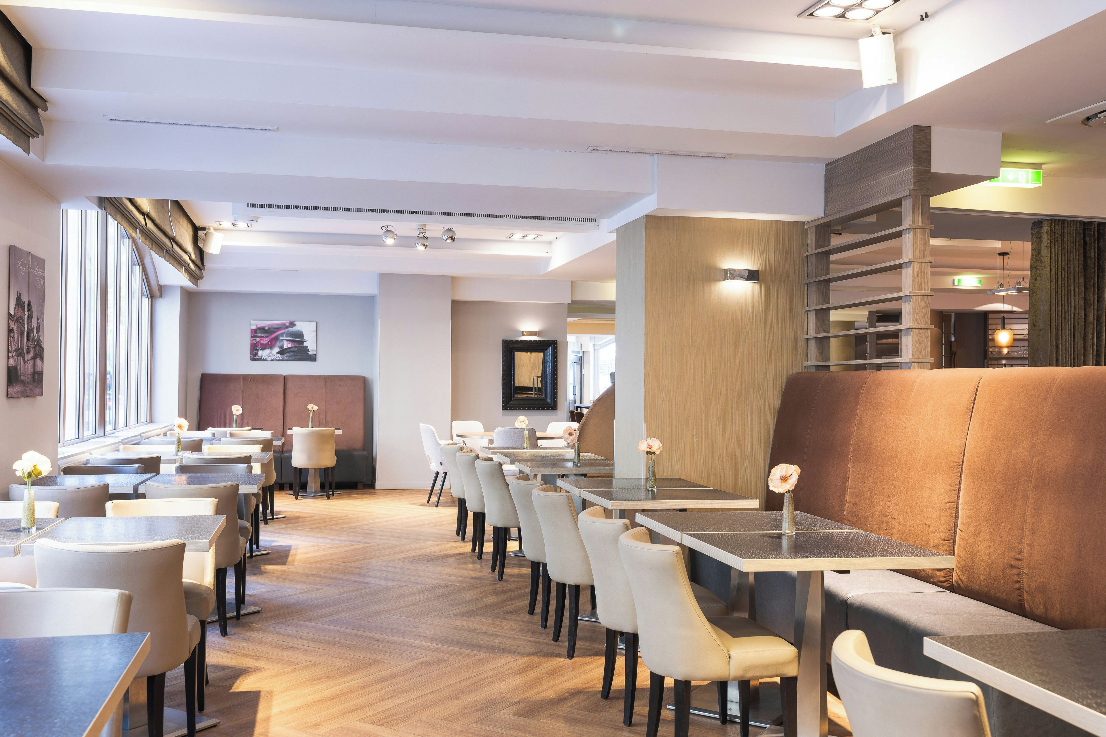 Een modern restaurantinterieur met meerdere eettafels en stoelen, een houten vloer en een ruime zithoek met een comfortabele bank.
