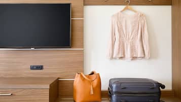 Habitación de hotel con un aparador de madera, un televisor montado en la pared, una prenda colgada, un bolso marrón y una maleta azul.
