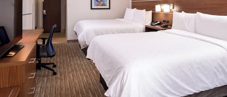 A hotel room with two beds, a desk with a computer, a chair, and a bedside table with a phone and lamp.