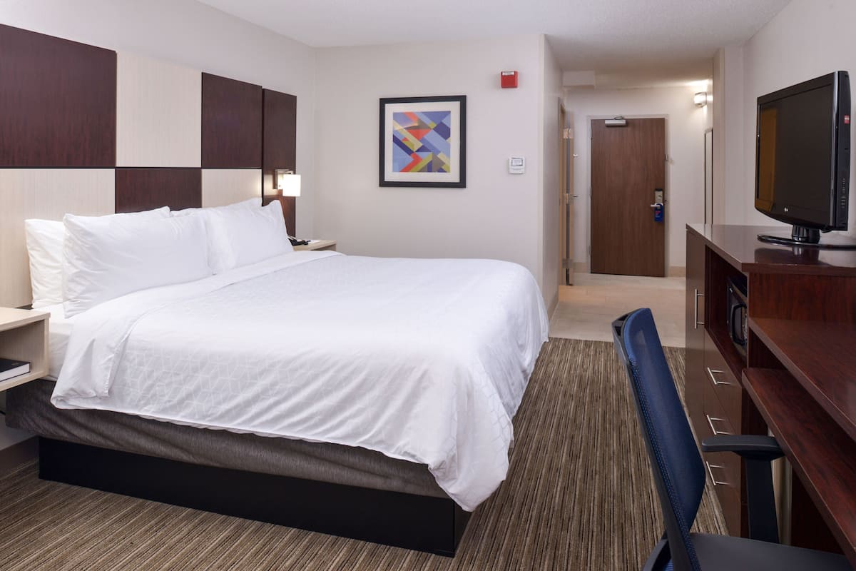 A hotel room with a large bed, a desk with a television, and a door leading to a hallway.