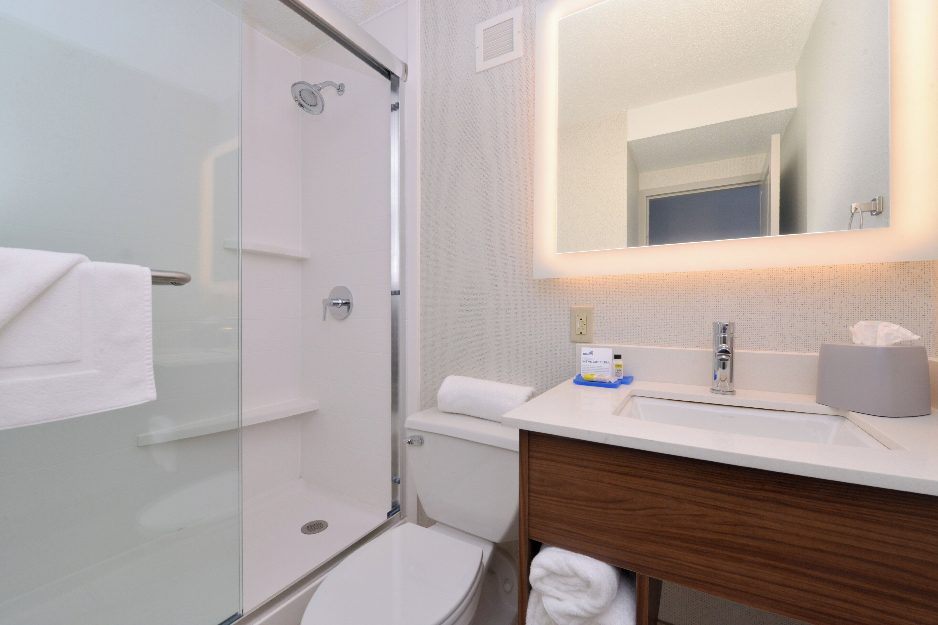 A modern bathroom with a glass shower enclosure, a white toilet, a sink with a mirror, and a wooden vanity.