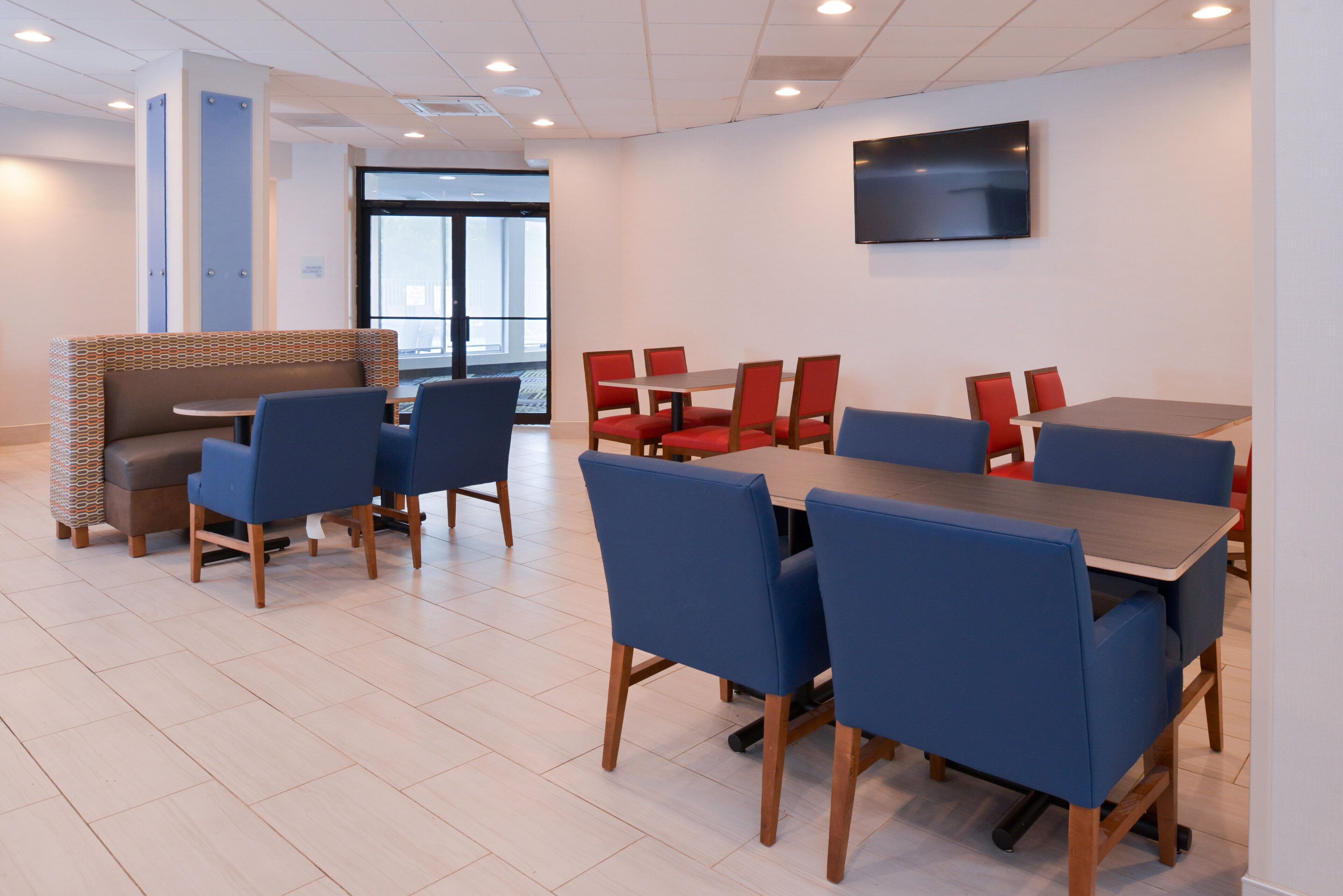 Un área de comedor moderna con sillas azules y rojas, una mesa de madera y un televisor montado en la pared.