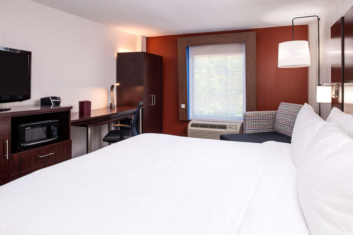 A hotel room with a bed, a desk with a microwave, a television, and a window with blinds.