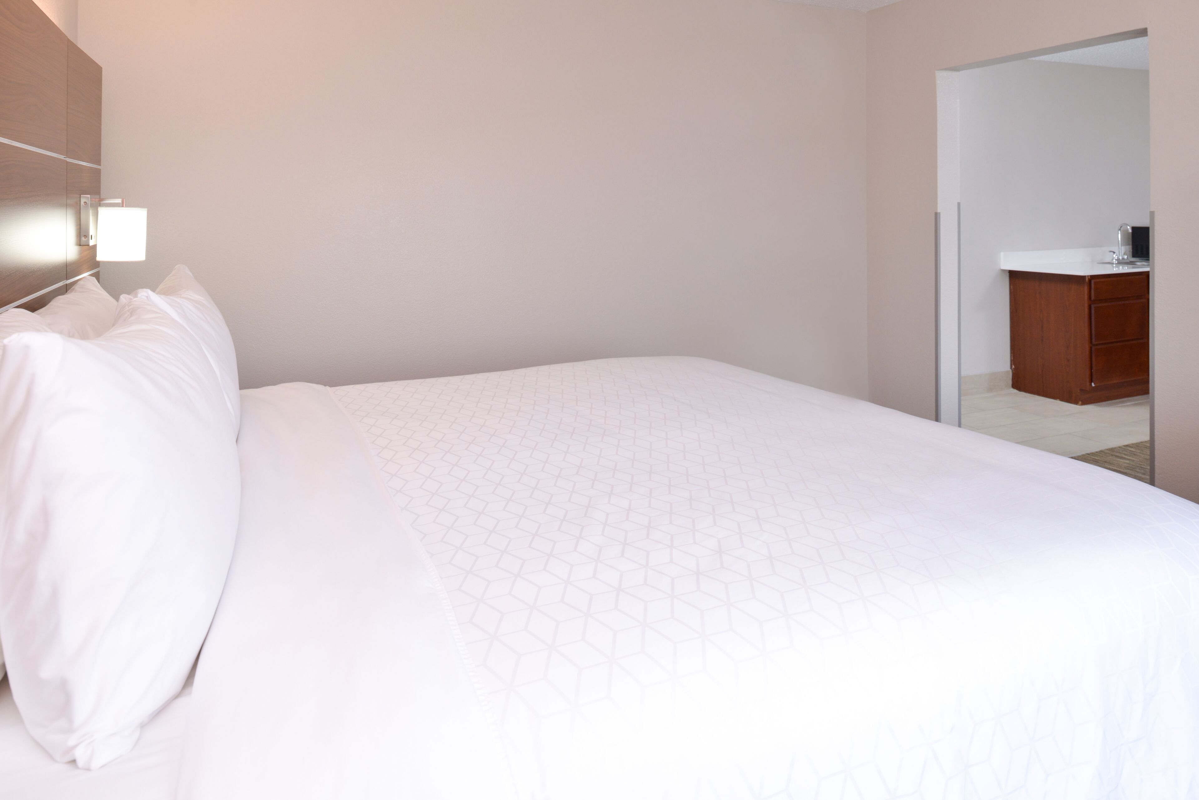 Una habitación de hotel con una cama grande, un cabecero de madera, una mesita de noche y un baño pequeño a la vista a través de una puerta abierta.