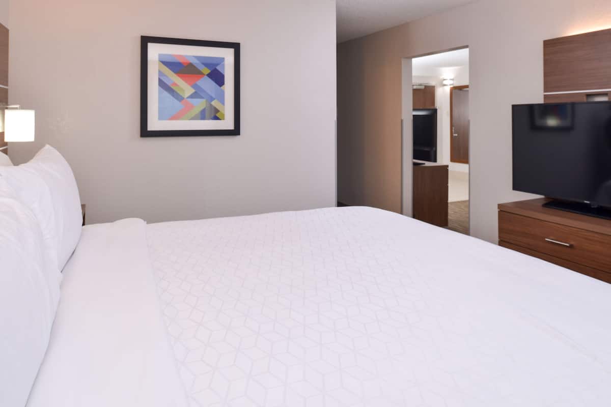 A hotel room with a large bed, a flat-screen TV, a framed abstract painting, and a wooden cabinet.