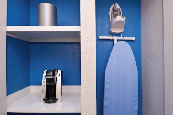 A bathroom with a coffee machine, an iron, and a shelf with a cylindrical container.
