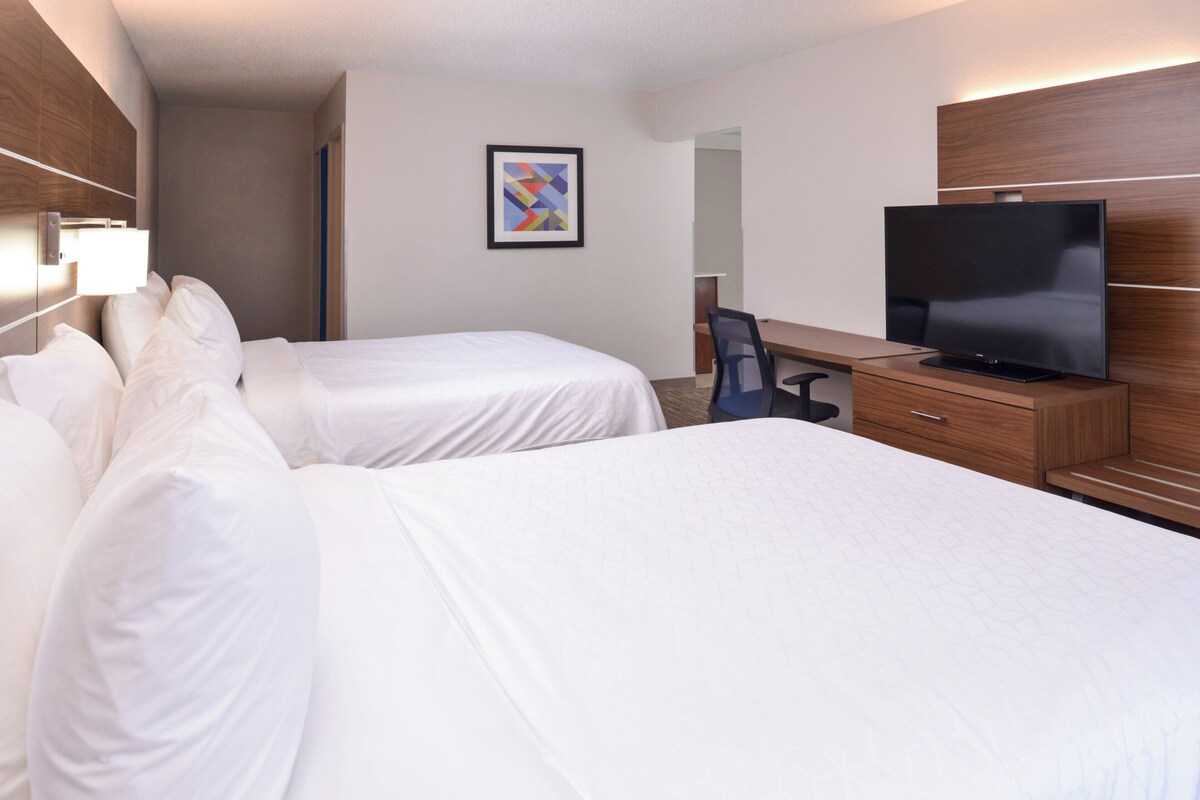 A hotel room with two beds, a desk, a television, and a framed artwork on the wall.