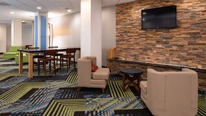 A modern hotel lobby with a stone wall, a flat-screen TV, a dining area with a table and chairs, and a patterned carpet. - Holiday Inn Express Towson - Baltimore North by IHG (Towson)