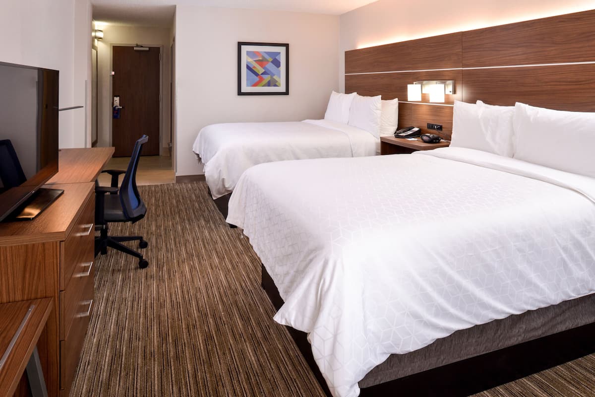 A hotel room with two beds, a desk with a chair, a TV, and a framed picture on the wall.