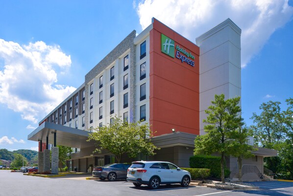 A Holiday Inn Express building with a red and white facade, multiple floors, and a parking lot with several cars.