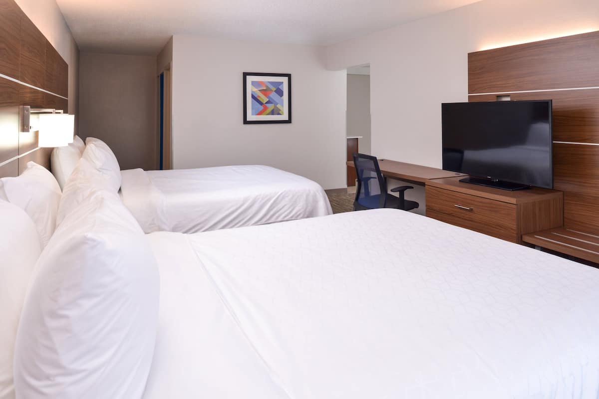 A hotel room with two beds, a desk, a television, and a framed artwork on the wall.