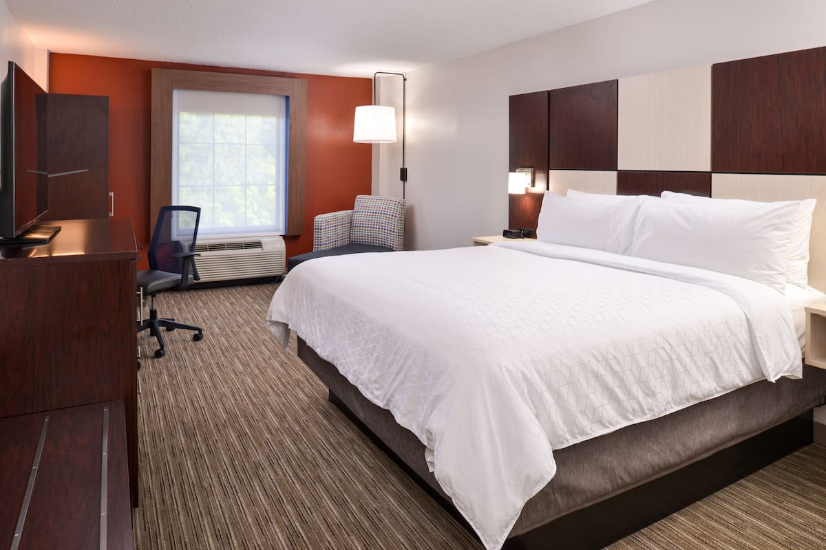 A hotel room with a large bed, a desk with a chair, a television, and a window with blinds.