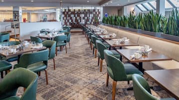 A modern dining area with green upholstered chairs, wooden tables, and a patterned carpet.