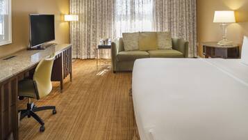A hotel room with a bed, a desk with a chair, a television, a sofa, and a small table with a lamp.