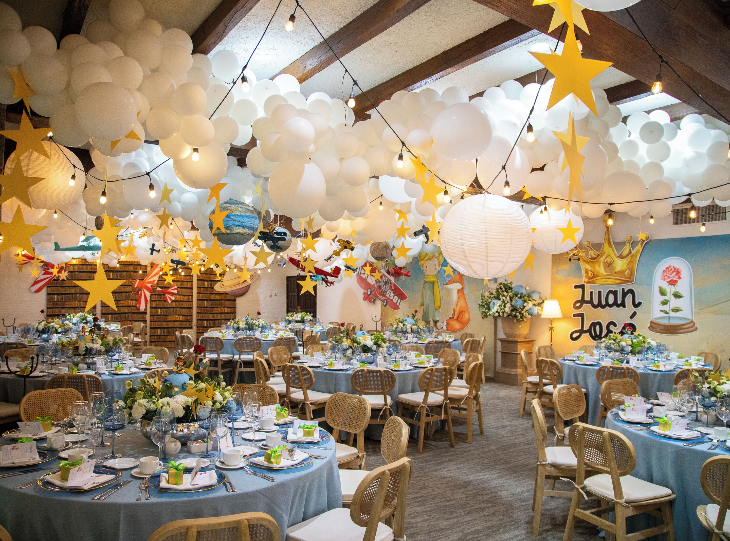 Ein Bankettsaal mit runden Tischen, gedeckt für eine festliche Veranstaltung, mit einer Decke, die mit Ballons und Sterndekorationen verziert ist.