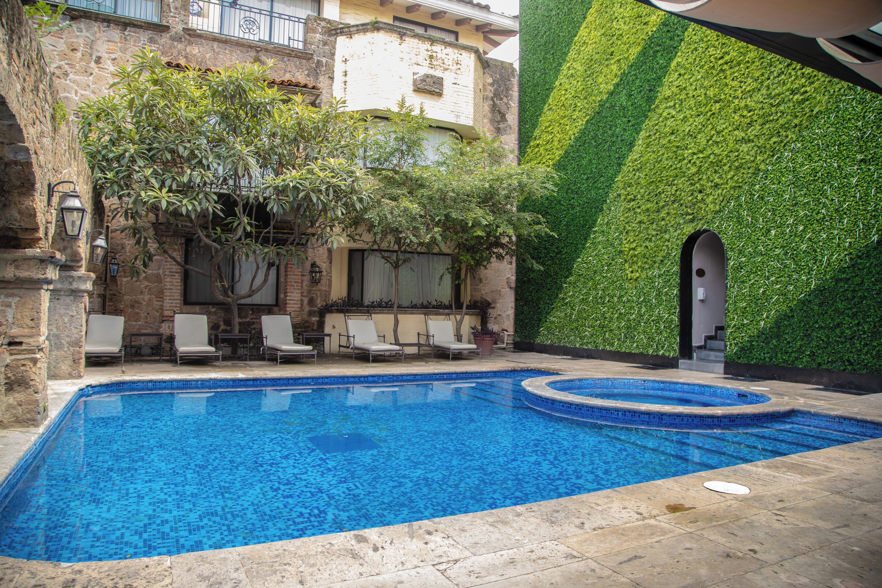Una piscina con sillones de descanso y una pared verde.