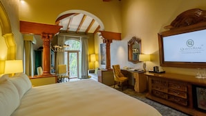 Habitación de hotel con una cama grande, un escritorio con silla, televisión y minibar.
