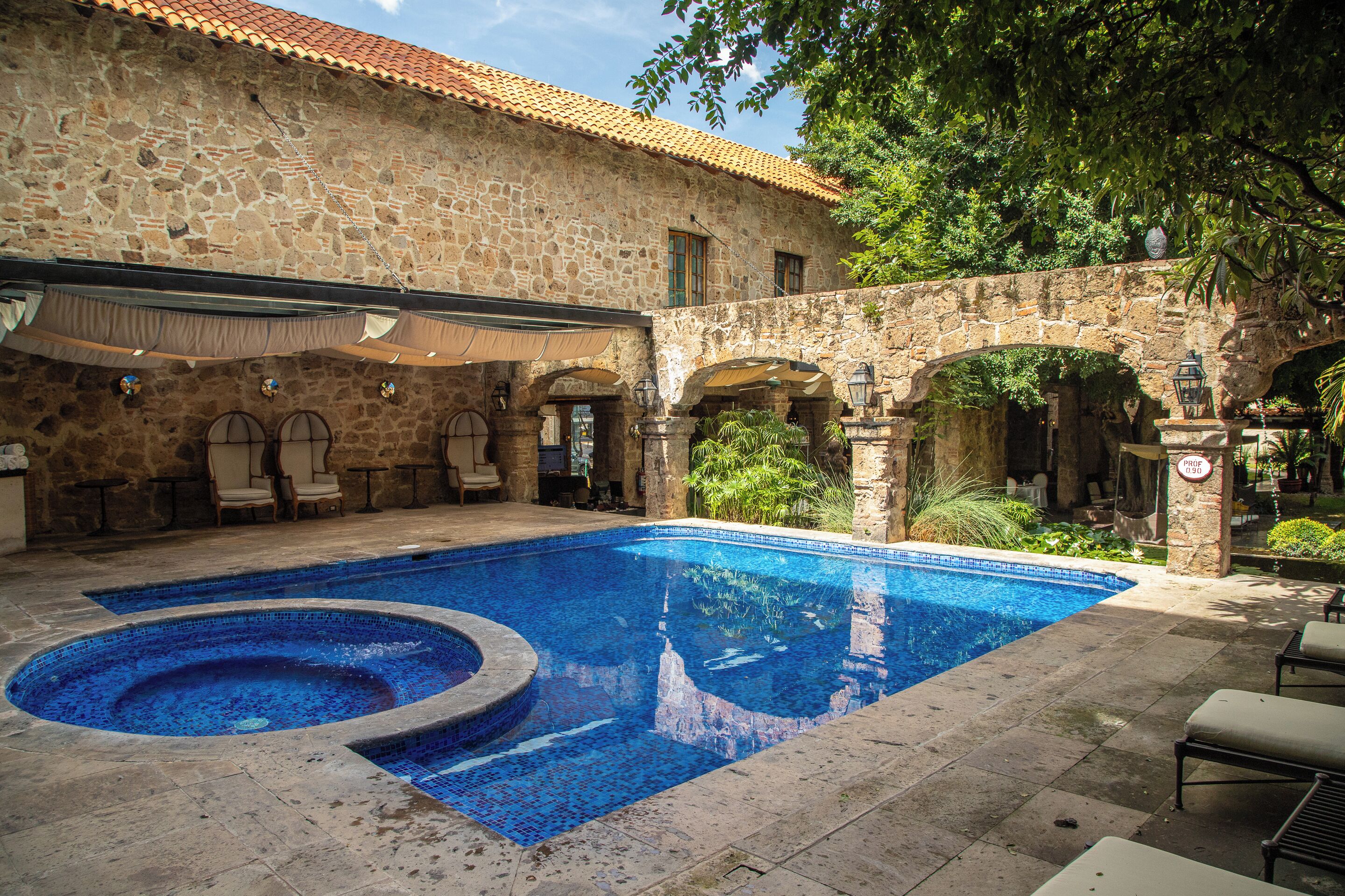 Un edificio de piedra con piscina, mobiliario exterior y vegetación.