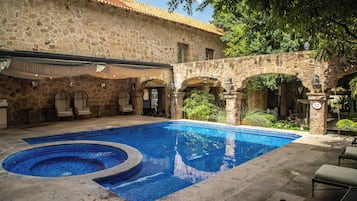 Un edificio de piedra con piscina, mobiliario exterior y vegetación.