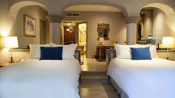A hotel room with two beds, a desk, a mirror, and a bathroom visible through an archway.