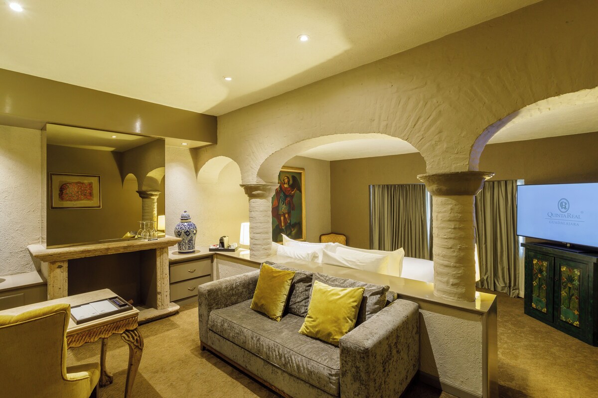 Una habitación de hotel con sofá, escritorio, televisor y un espejo grande.