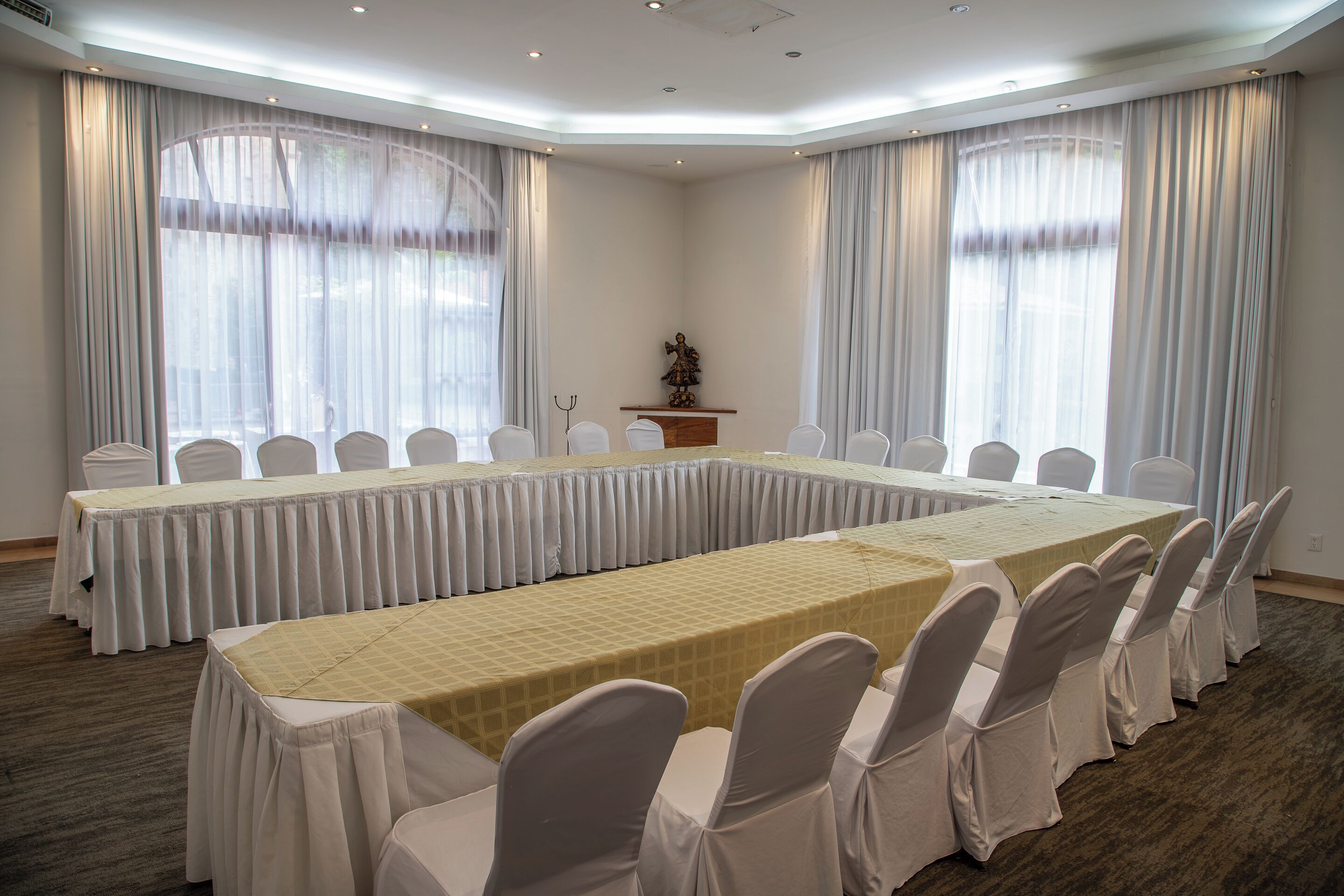 Un salón de conferencias con una larga mesa y sillas, ventanas grandes con cortinas y un atril.