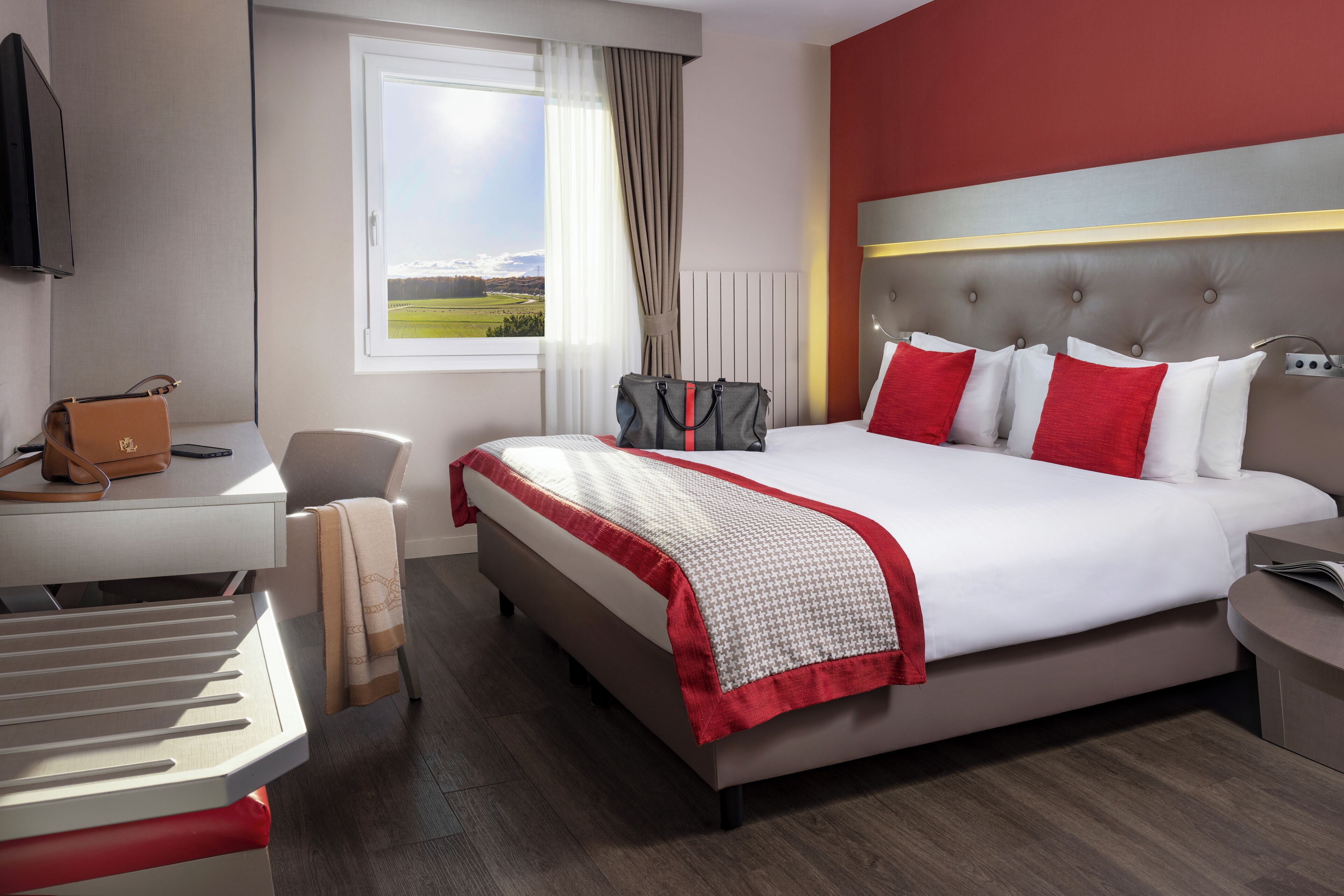 Een hotelkamer met een bed, een bureau, een stoel, een raam met uitzicht en een televisie.