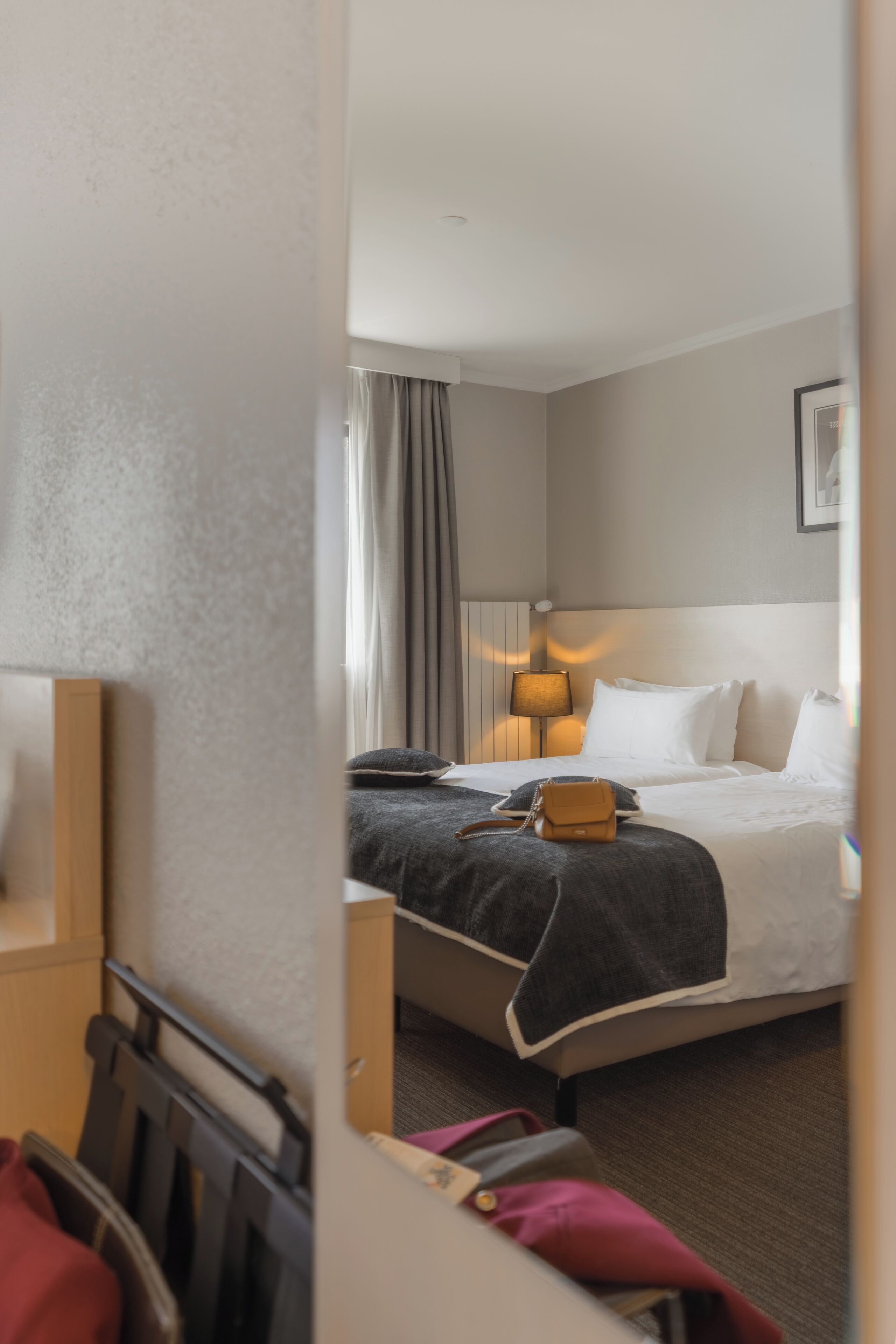 Habitación de hotel con cama, mesita de noche, lámpara y ventana con cortinas.
