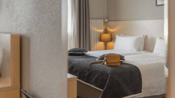 Habitación de hotel con cama, mesita de noche, lámpara y ventana con cortinas.