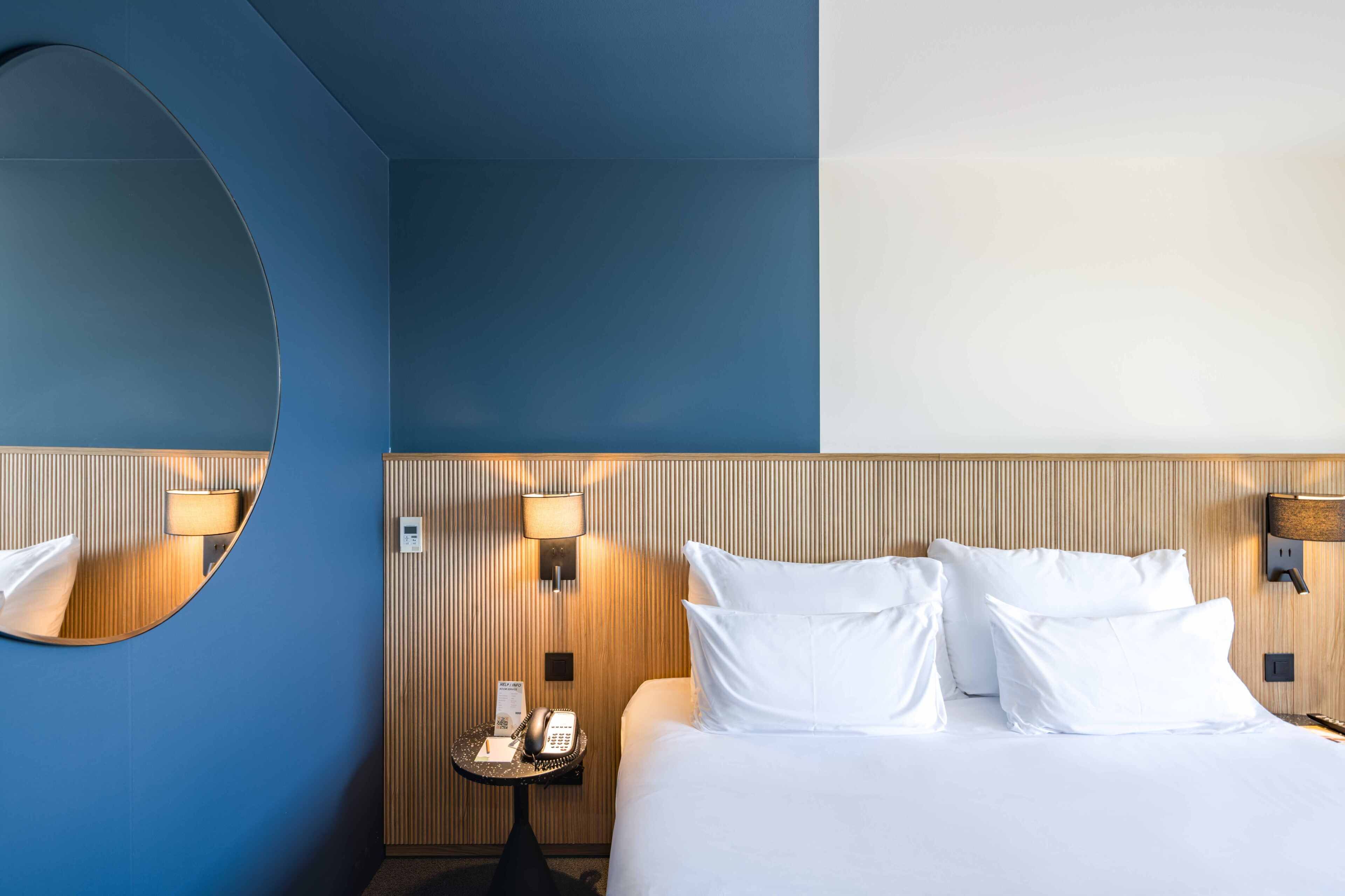 A hotel room with a large bed, a round mirror, and a wall-mounted telephone.