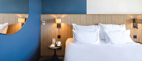 A hotel room with a large bed, a round mirror, and a wall-mounted telephone.