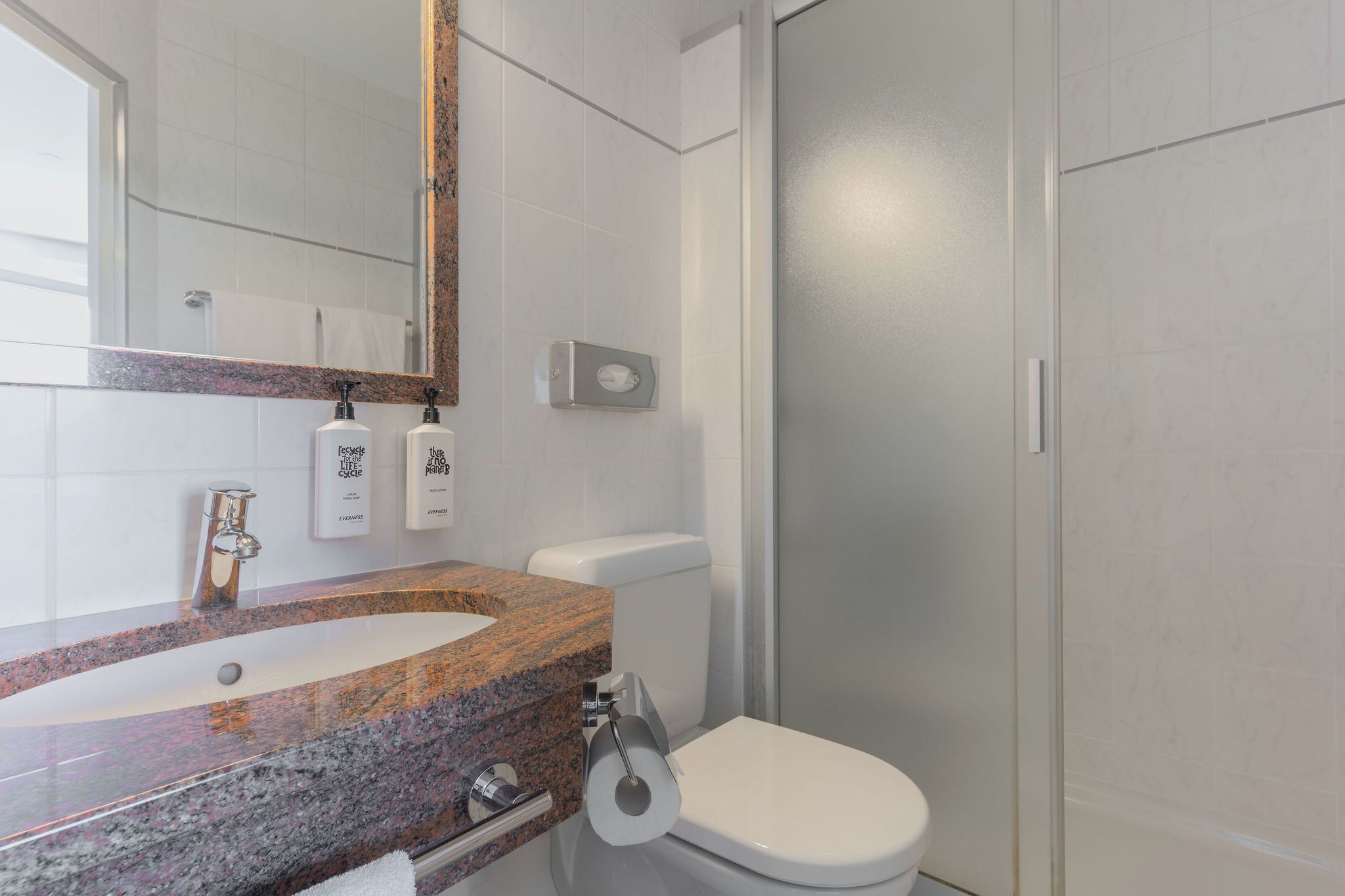 A bathroom with a granite countertop, a toilet, and a shower enclosure.