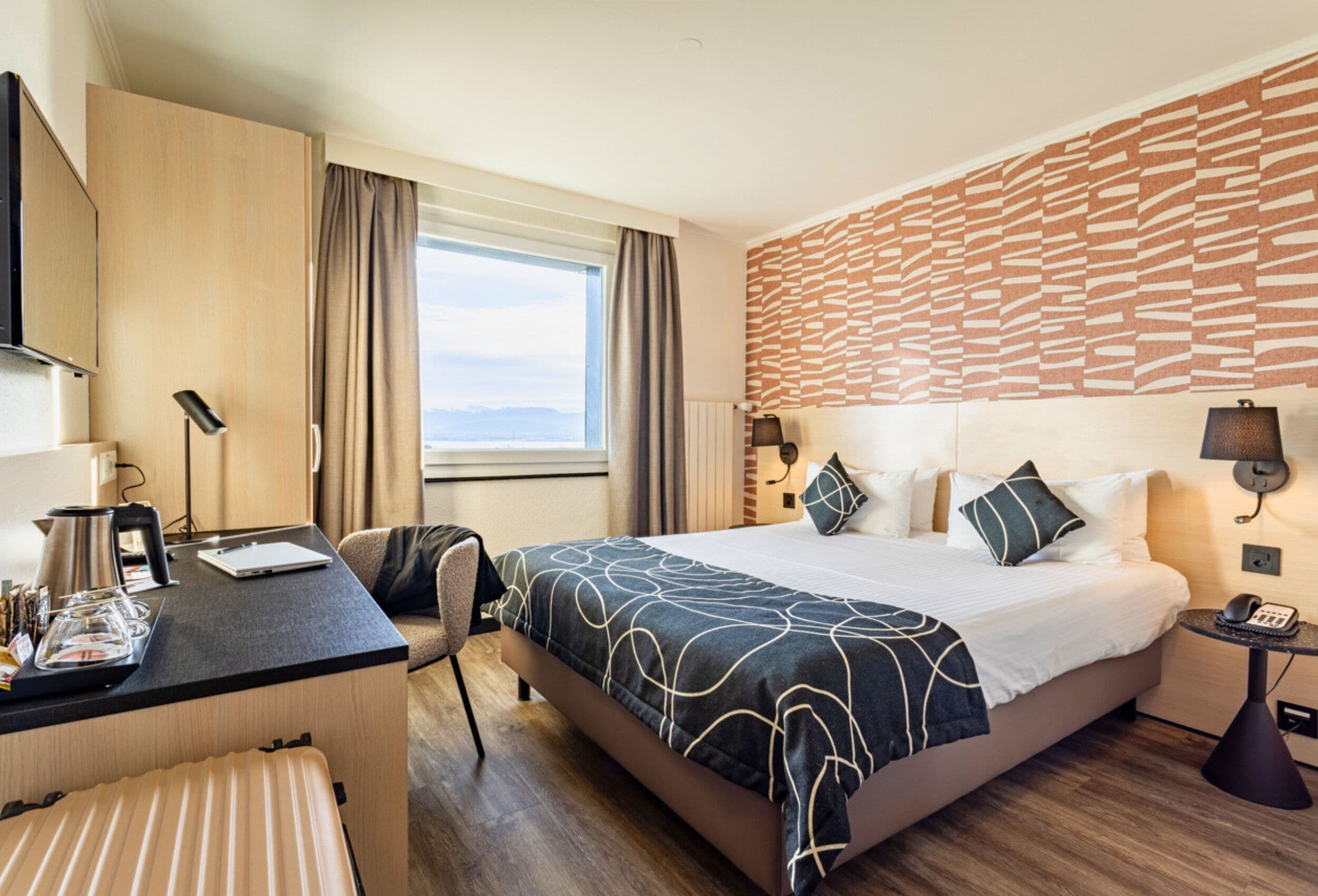 A hotel room with a bed, desk, chair, and a view of the outdoors.