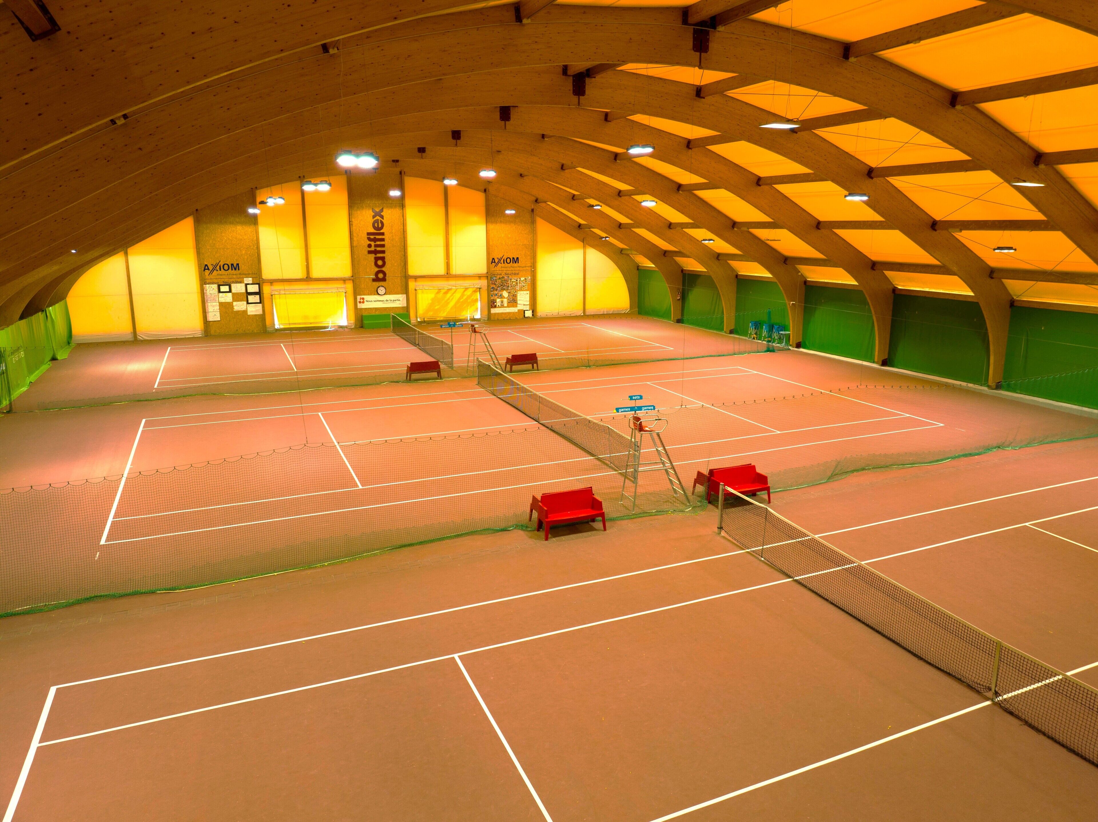 An indoor tennis court with multiple courts, a net, and seating areas.