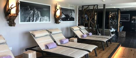 Un espacio de spa con tumbonas de madera, obras de arte en la pared y suelo de madera.