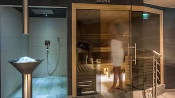 Un sauna avec une porte en verre, un seau en métal rempli de glace et un banc en bois.