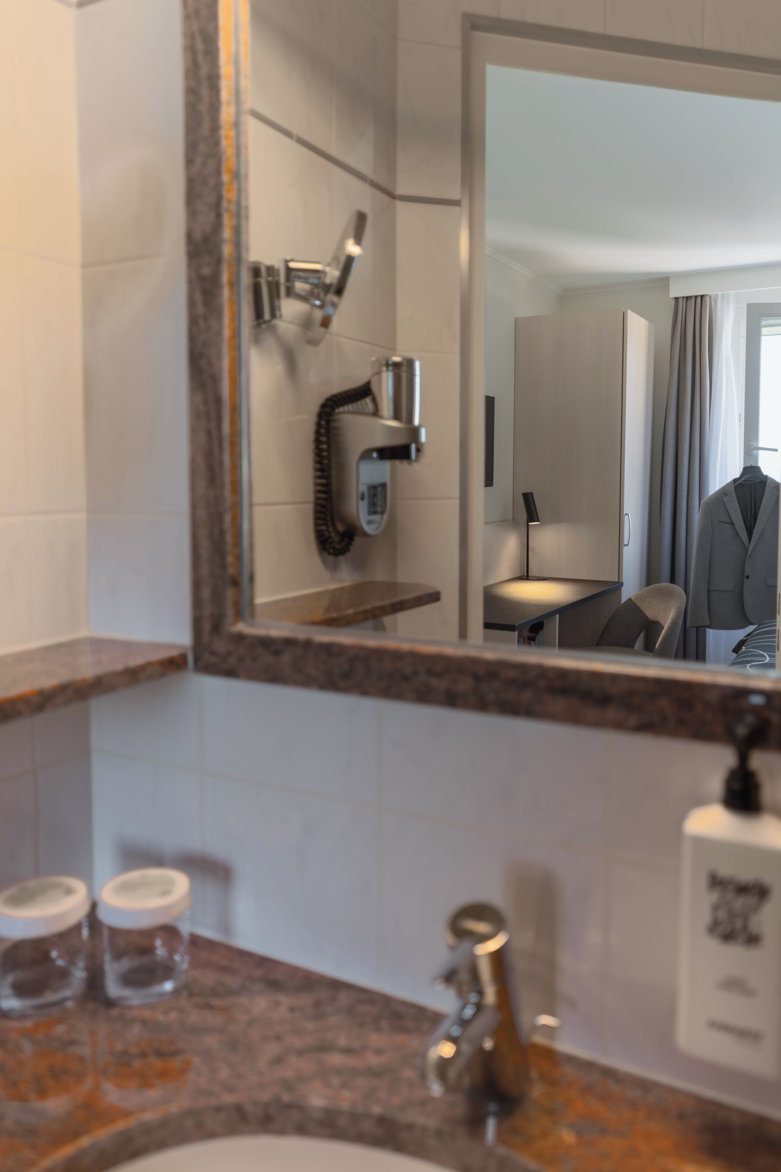 Un bagno con top in marmo, lavandino, specchio, porta asciugamani e doccia.
