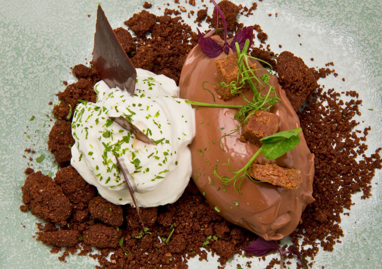 Un dessert composé de crème fouettée, de chocolat et de diverses garnitures, présenté sur une assiette à texture particulière.