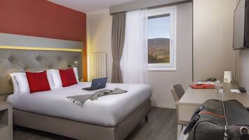 A hotel room with a bed, a desk, a laptop, and a view of the outdoors.