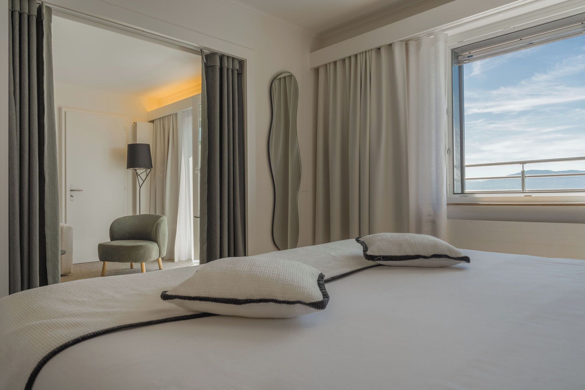 Ein Hotelzimmer mit einem großen Bett, einem Sessel, einer Stehlampe und Meerblick.