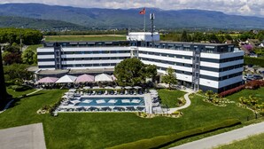 A modern hotel with a swimming pool, surrounded by lush greenery and mountains in the background.