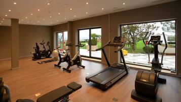 Een sportschool met diverse fitnessapparaten, grote ramen en uitzicht op het buiten.