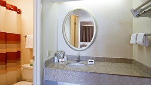 Une salle de bain avec des toilettes, un lavabo et un miroir. On y trouve également un porte-serviettes et un rideau de douche.