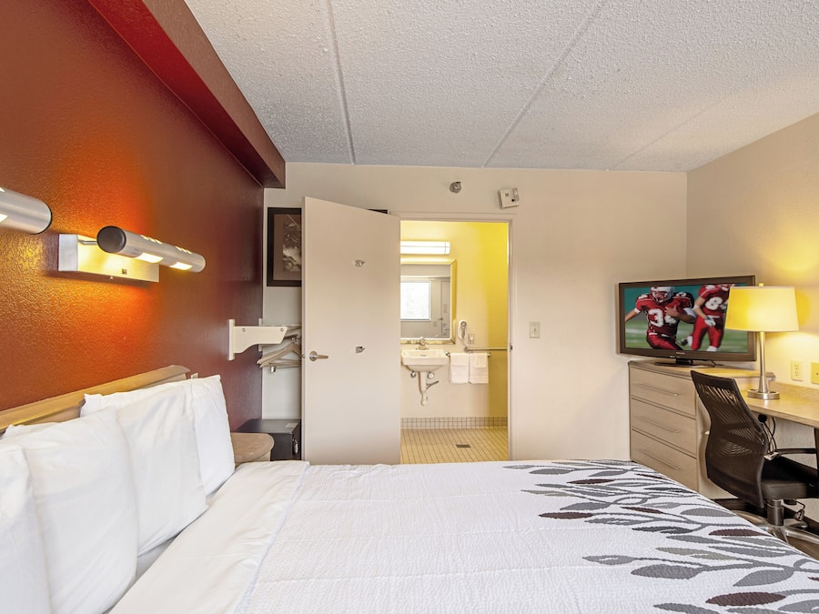 A hotel room with a bed, a desk, a chair, a television, and a bathroom visible through an open door.