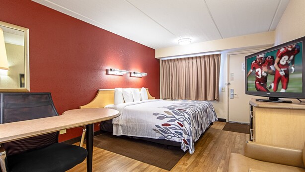 A hotel room with a bed, a desk, a chair, a television, and a window with curtains. - Red Roof Inn Charleston West - Hurricane, WV (Hurricane)