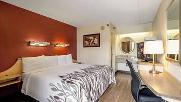Una habitación de hotel con cama, escritorio, silla, espejo y televisor.
