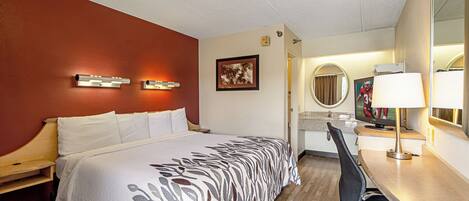 A hotel room with a bed, a desk, a chair, a mirror, and a television.
