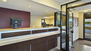 A reception desk with a computer monitor, a cash register, and a telephone. There is a glass door leading to a hallway. - Red Roof Inn Charleston West - Hurricane, WV (Hurricane)