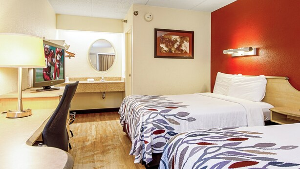 A hotel room with a desk, two beds, a mirror, and a red accent wall. - Red Roof Inn Charleston West - Hurricane, WV (Hurricane)